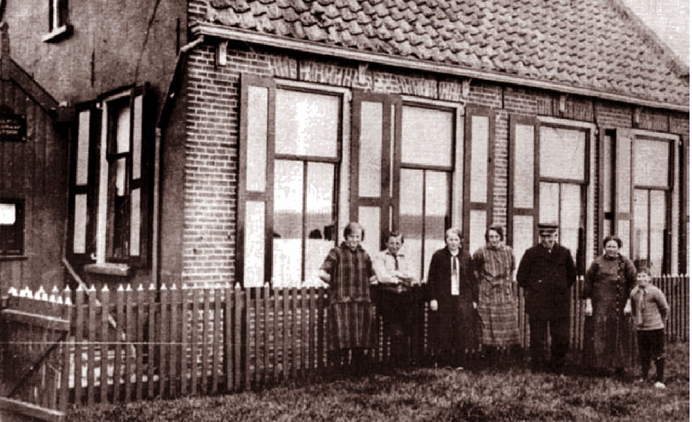 De familie H. Smit voor hun woning in Emmeloord. De derde persoon van links is de onderwijzeres van de kinderen, mejuffrouw Witkop. <2>